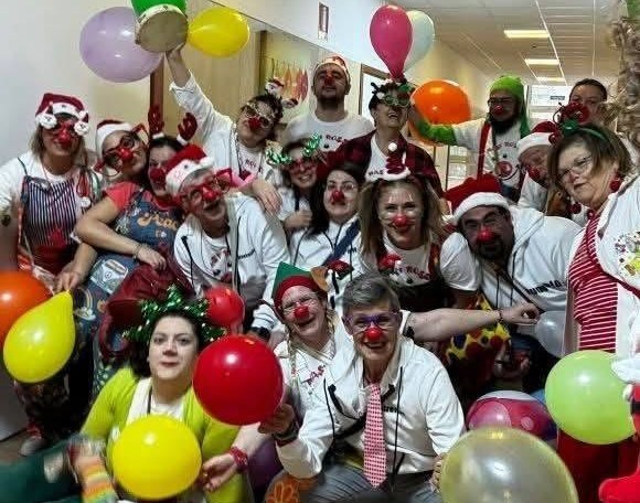 Il gruppo dei clown volontari con nasi rossi, cappelli di Babbo Natale e palloncini colorati nel corridoio di un reparto